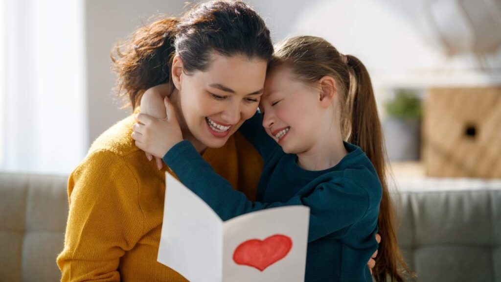 mãe segurando uma carta com um desenho de coração enquanto sua filha rir ao seu lado